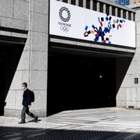 A man wearing a protective face mask walks past banners promoting the 2020 Tokyo Olympic Games outside the Tokyo Metropolitan Government building in the capital in March last year. | NORIKO HAYASHI/THE NEW YORK TIMES