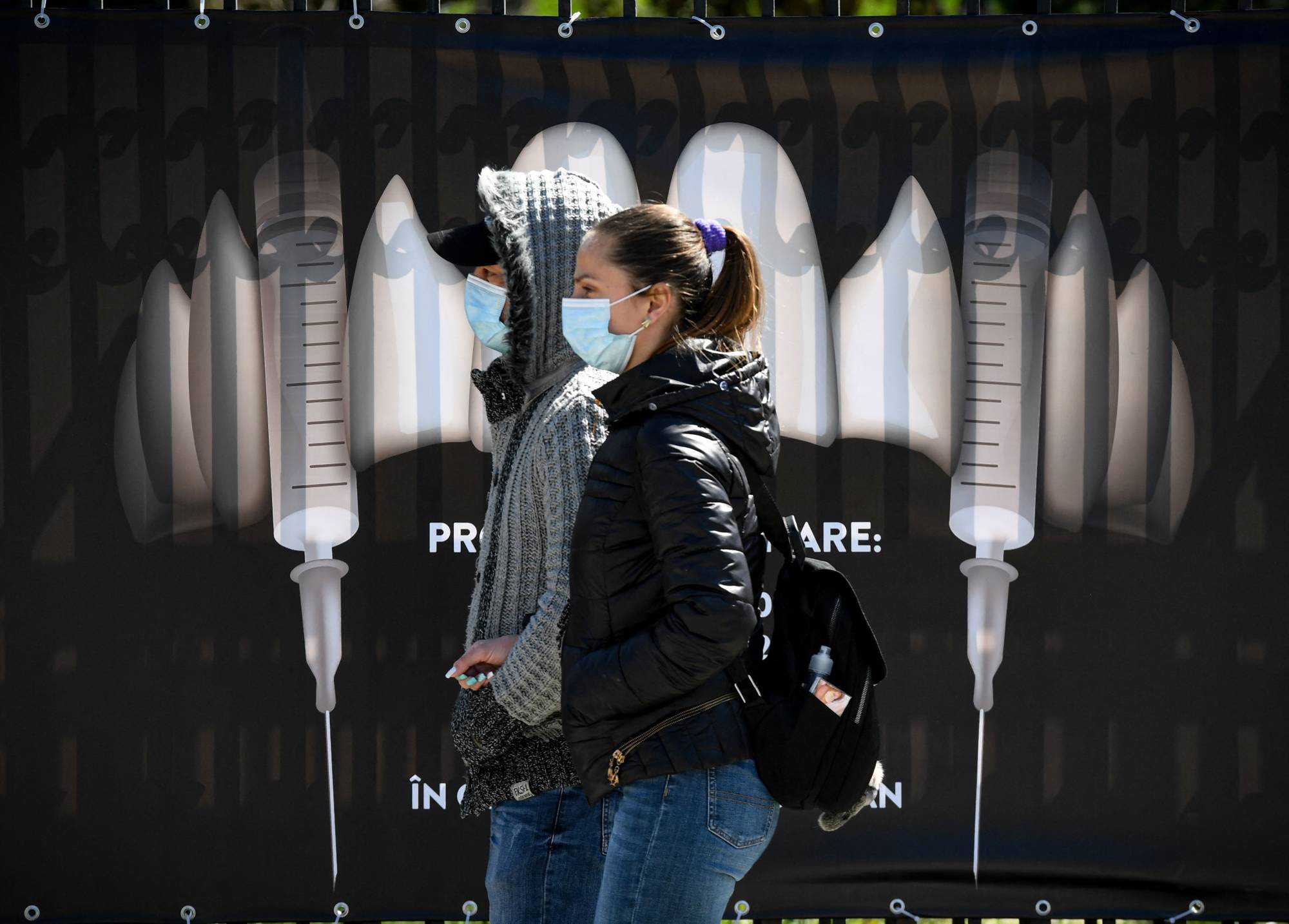 People wearing masks walk by a banner showing syringes as vampire fangs at a vaccination center at Bran Castle  — purported to be an inspiration for the vampire's towering home in Bram Stoker’s novel 'Dracula'  — in Bran, Romania, on Saturday. | AFP-JIJI