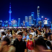 People walk near the Bund, as Shanghai\'s Lujiazui financial district is seen in the background, on Monday. China on Tuesday announced its slowest population growth since the 1950s, sharply reducing the size of the labor force as the nation ages, and worsening demographic pressures in the economy. | REUTERS
