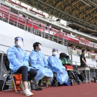 Staff members wearing masks and face shields sit in the National Stadium in Tokyo on Sunday during a track and field test event for this summer\'s Tokyo Olympics. | KYODO