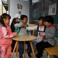 Children play outside a cafe in Beijing on Tuesday. Because it’s betting on productivity gains, demographers don’t expect China’s government to launch an all-out effort to raise births. | AFP-JIJI