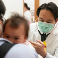 Toshikatsu Mitsui examines a baby prior to administering a routine vaccination at Muza Kawasaki Pediatric Clinic in Kawasaki, Kanagawa Prefecture. | ROB GILHOOLY