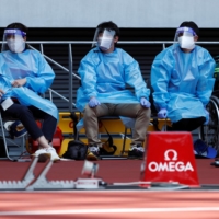 Medical officers wearing protective suits watch an athletics test event at National Stadium on Sunday. | REUTERS