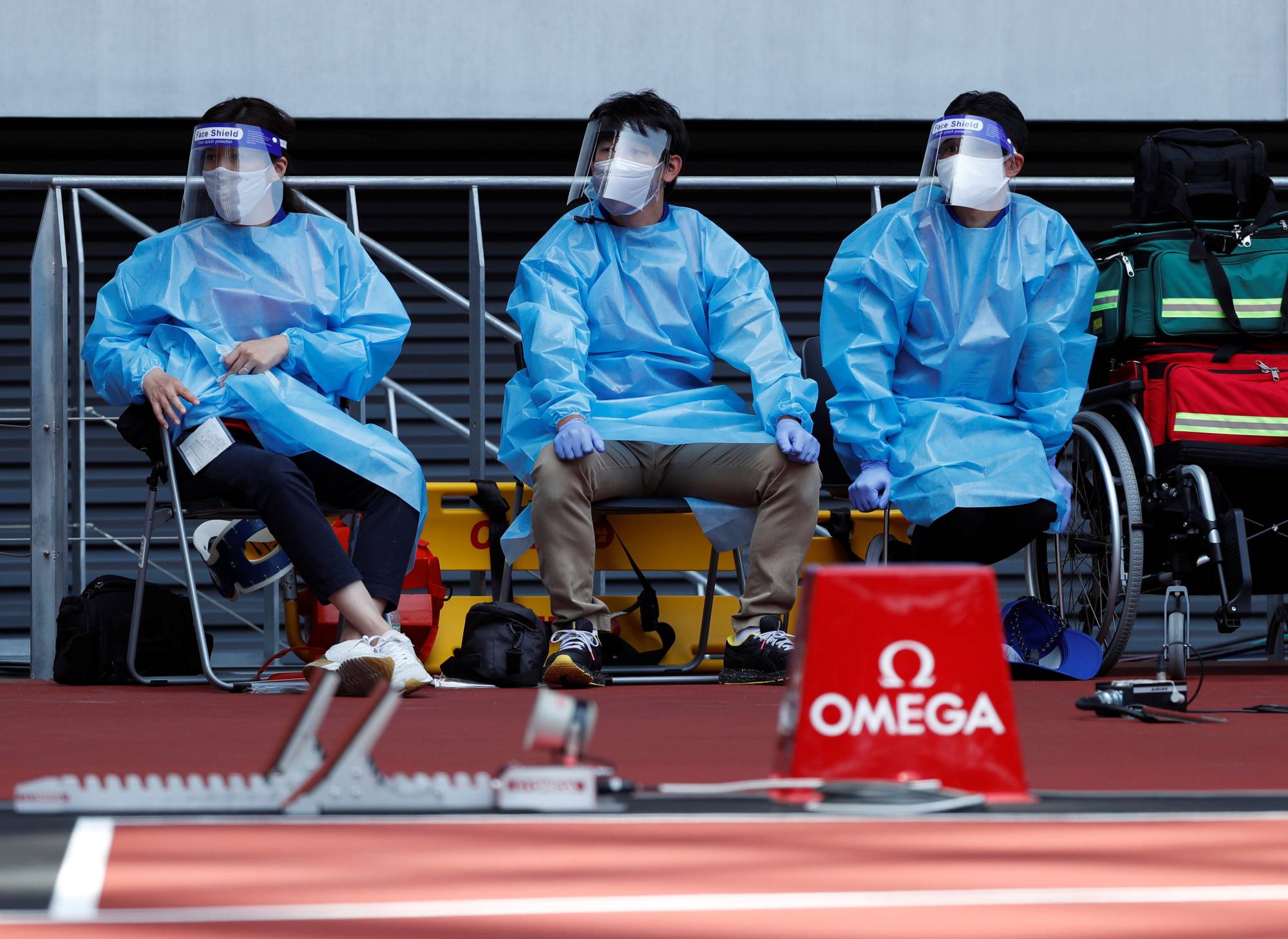 Medical officers wearing protective suits watch an athletics test event at National Stadium on Sunday. | REUTERS