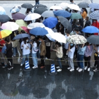 People line up in the rain to get vaccinated against the coronavirus outside an inoculation site in Fuyang, in China\'s Anhui province, on Saturday.  | CHINA DAILY / VIA REUTERS  