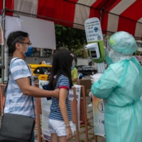 A health care worker checks the temperature of a girl entering a COVID-19 testing site in Taipei on Monday. | BLOOMBERG 