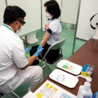 A staff member and a participant take part in a coronavirus vaccination simulation by the Self-Defence Forces at an inoculation center in Tokyo on Friday. | AFP-JIJI