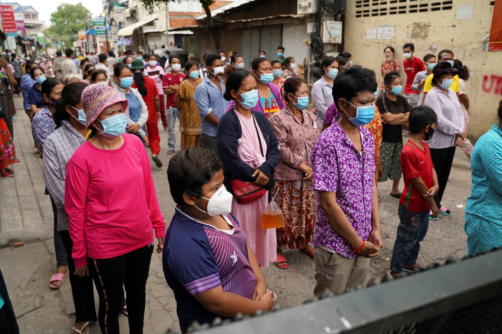 People stand behind a lockdown barrier to ask for food donations after their village had been closed for more than two weeks as part of anti-COVID-19 measures near Phnom Penh on April 30. | REUTERS 