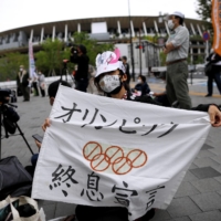 Anti-Olympics protester shows off a banner with the National Stadium in the background outside the Japanese Olympic Committee\'s headquarters during a rally in Tokyo last week. | REUTERS