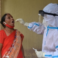 A health worker collects a swab sample from a woman to test for the coronavirus at a primary health center in Siliguri, India, on Monday. | AFP-JIJI