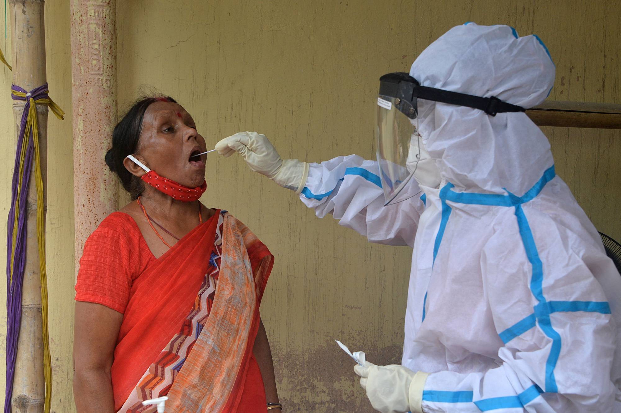 A health worker collects a swab sample from a woman to test for the coronavirus at a primary health center in Siliguri, India, on Monday. | AFP-JIJI