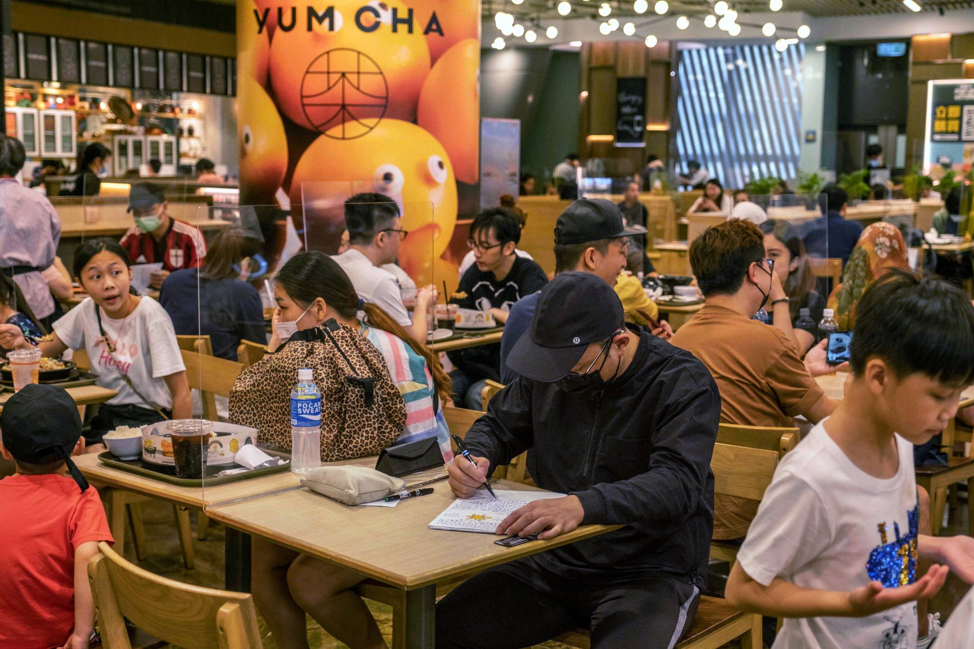 Daniel Tang, who spent time in prison for his role in Hong Kong’s pro-democracy protests in 2019, works on letters to activists currently behind bars while at a food court in Hong Kong on Sunday.  | LAM YIK FEI / THE NEW YORK TIMES