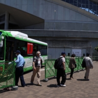 People arrive via a bus to receive a dose of the Pfizer-BioNTech COVID-19 vaccine at a mass-inoculation site at Noevir Stadium Kobe on Tuesday. After some false starts, Japan\'s much-delayed vaccine rollout is quietly picking up steam, now administering between 400,000 and 500,000 doses a day.  | BLOOMBERG