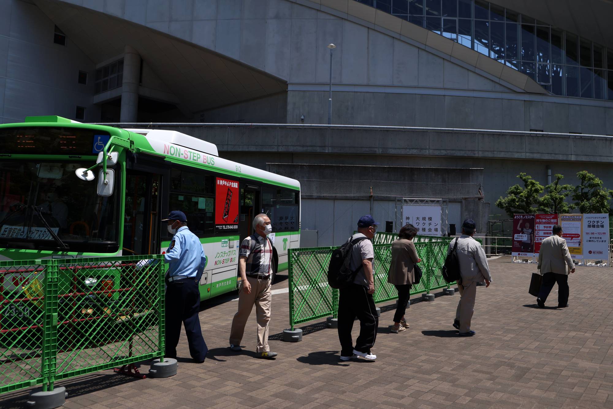 People arrive via a bus to receive a dose of the Pfizer-BioNTech COVID-19 vaccine at a mass-inoculation site at Noevir Stadium Kobe on Tuesday. After some false starts, Japan's much-delayed vaccine rollout is quietly picking up steam, now administering between 400,000 and 500,000 doses a day.  | BLOOMBERG