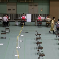 A woman in a wheelchair arrives to receive a dose of the Pfizer-BioNTech COVID-19 vaccine at an inoculation site at Miyakojima Sports Center in the city of Osaka on Tuesday. After some false starts, Japan\'s much-delayed vaccine rollout is quietly picking up steam, now administering between 400,000 and 500,000 doses a day.  | BLOOMBERG