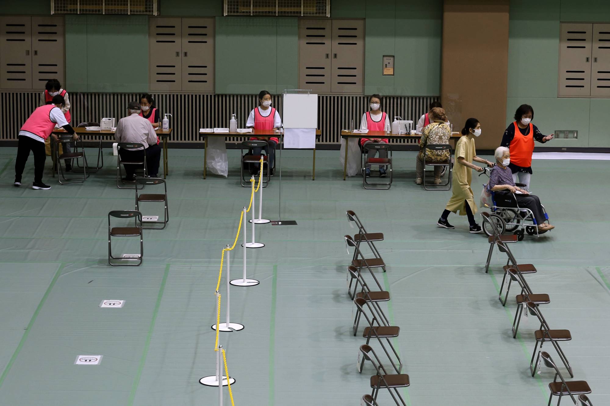 A woman in a wheelchair arrives to receive a dose of the Pfizer-BioNTech COVID-19 vaccine at an inoculation site at Miyakojima Sports Center in the city of Osaka on Tuesday. After some false starts, Japan's much-delayed vaccine rollout is quietly picking up steam, now administering between 400,000 and 500,000 doses a day.  | BLOOMBERG