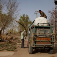 Wang Tianchang, 78, a veteran of China\'s state campaign to \"open up the wildernesls,\" helps his son, Wang Yinji, fill a water tank before driving into the desert to plant trees, at his house on the outskirts of Wuwei.  | REUTERS 
