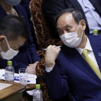 Prime Minister Yoshihide Suga confers with a staff member in the Diet\'s Upper House in Tokyo on June 7. | BLOOMBERG