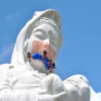 Workers place a mask on a 57-meter-tall Buddhist goddess statue to pray for the end of the coronavirus pandemic, at Houkokuji Aizu Betsuin in Aizuwakamatsu, Fukushima Prefecture, on Tuesday. | HOUKOKUJI AIZU BETSUIN / VIA REUTERS