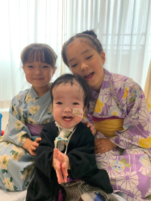 Yuto Kubo (center) and his sisters at their home in Tokyo's Setagaya Ward on May 5. Yuto uses an artificial respirator and a feeding tube. | COURTESY OF CHIHIRO KUBO / KYODO