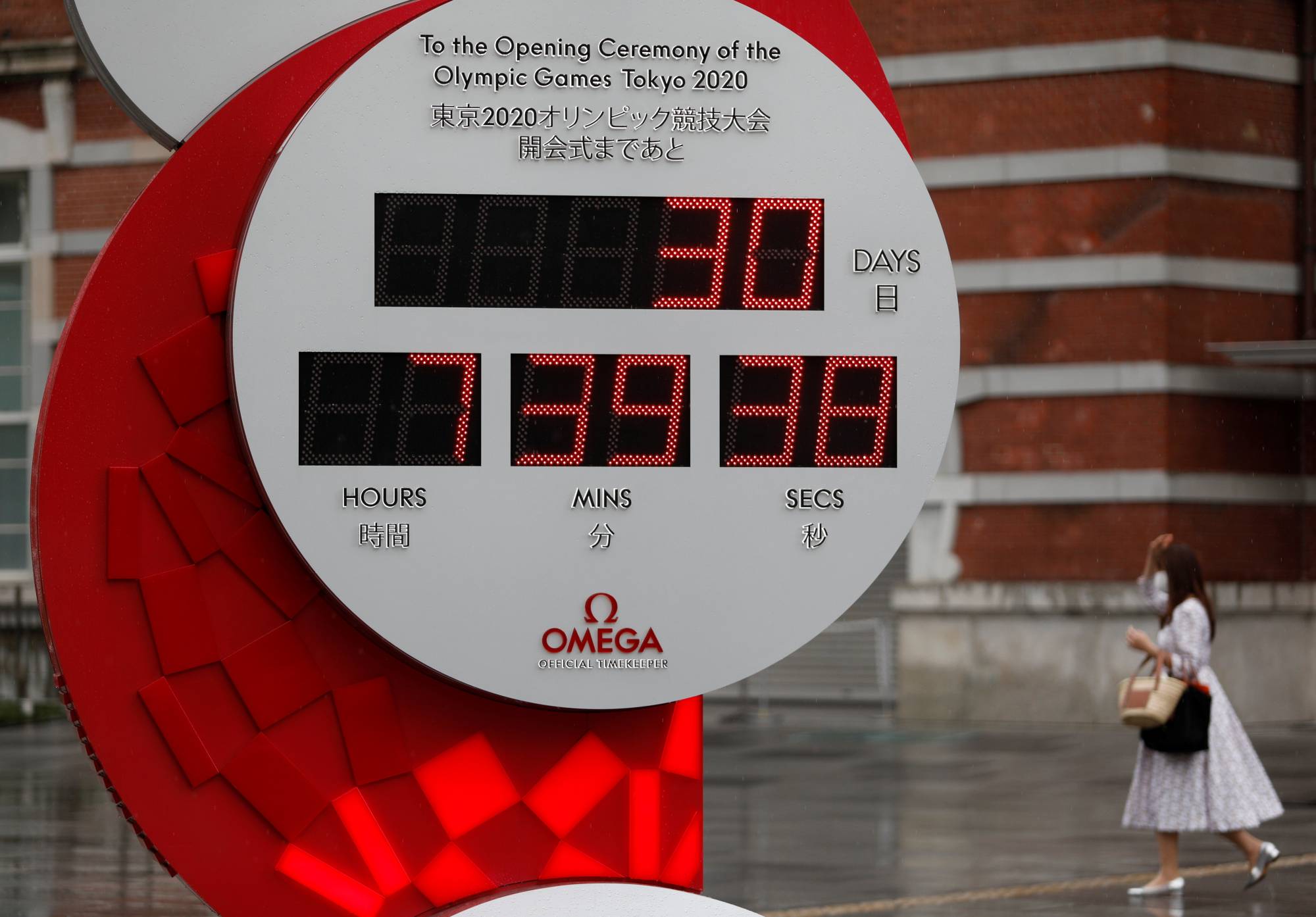 A woman walks near a countdown clock for the Tokyo Olympics in Tokyo on Wednesday, a month before the opening of the games. | REUTERS