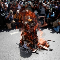 Members of the media take photos of a model of Democracy Monument set on fire by protesters in Bangkok on Thursday.  | REUTERS 