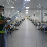 A worker holds a plastic divider inside a field hospital for Covid-19 patients at a park in Manila on June 24.  | AFP-JIJI