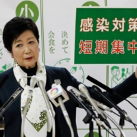 Tokyo Gov. Yuriko Koike holds a placard reading \"short-term intensive infection control measures,\" a slogan relating to the city\'s response to the coronavirus outbreak, at a news conference in Tokyo on Nov. 25. | REUTERS