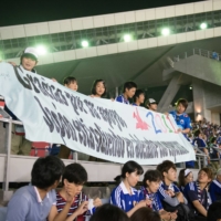Tohoku-area schoolchildren hold up a Spanish-language banner at an international friendly between Japan and Uruguay on Aug. 14, 2013, in Rifu, Miyagi Prefecture. | DAN ORLOWITZ