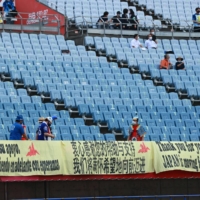 Japanese superfan Hirokazu Tsunoda (bottom center) and other volunteers arrange banners inside Miyagi Stadium before a pair of Olympic women\'s soccer games on Wednesday in Rifu, Miyagi Prefecture. | AFP-JIJI