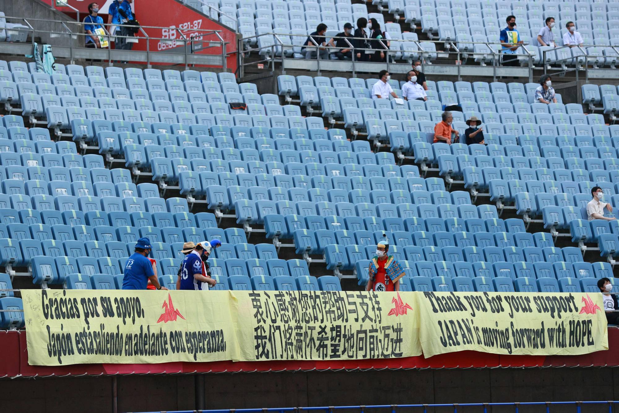Japanese superfan Hirokazu Tsunoda (bottom center) and other volunteers arrange banners inside Miyagi Stadium before a pair of Olympic women's soccer games on Wednesday in Rifu, Miyagi Prefecture. | AFP-JIJI
