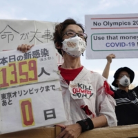 Protesters hold signs against holding the Olympics Games prior to the opening ceremony in Tokyo on Friday. | KYODO