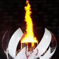 Tennis player Naomi Osaka, competing for Japan, stands with a torch after lighting the Olympic flame during the opening ceremony of the postponed 2020 Tokyo Olympics. | DOUG MILLS / THE NEW YORK TIMES