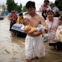 A man holding a baby wades through a flooded road following heavy rainfall in Zhengzhou, Henan province, China, on Thursday. | REUTERS