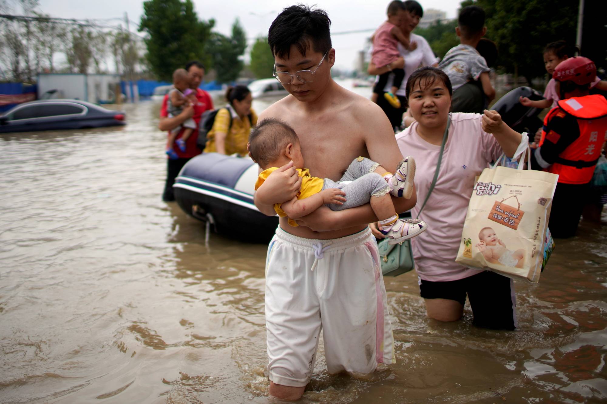 A man holding a baby wades through a flooded road following heavy rainfall in Zhengzhou, Henan province, China, on Thursday. | Reuters