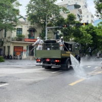 Men wearing personal protective equipment disinfect a street in Hanoi on Monday. The city is under lockdown amid an outbreak of COVID-19. | REUTERS