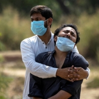 A man is consoled by a relative as he sees the body of his father, who died from complications related to COVID-19, before his burial in New Delhi in April.  | REUTERS 