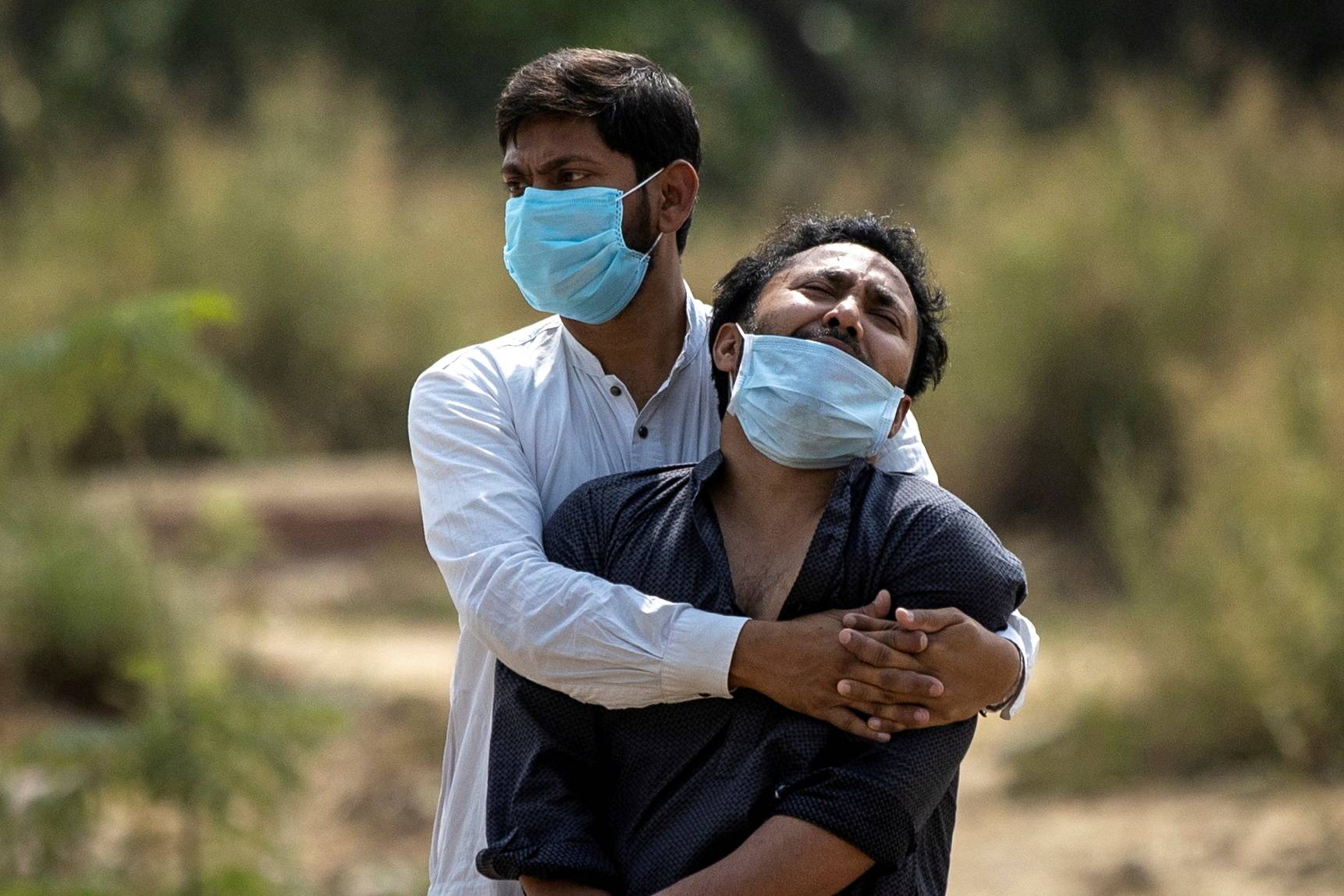A man is consoled by a relative as he sees the body of his father, who died from complications related to COVID-19, before his burial in New Delhi in April. | Reuters 