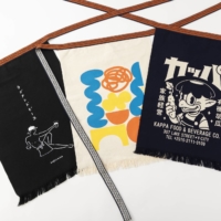 Anything Co. Ltd’s new lineup of maekake aprons features the work of three international artists (left to right): Whosming’s line art, Micke Lindebergh’s abstract work and Yeaaah! Studio’s retro-style brand logo. | HIROYUKI HARA
