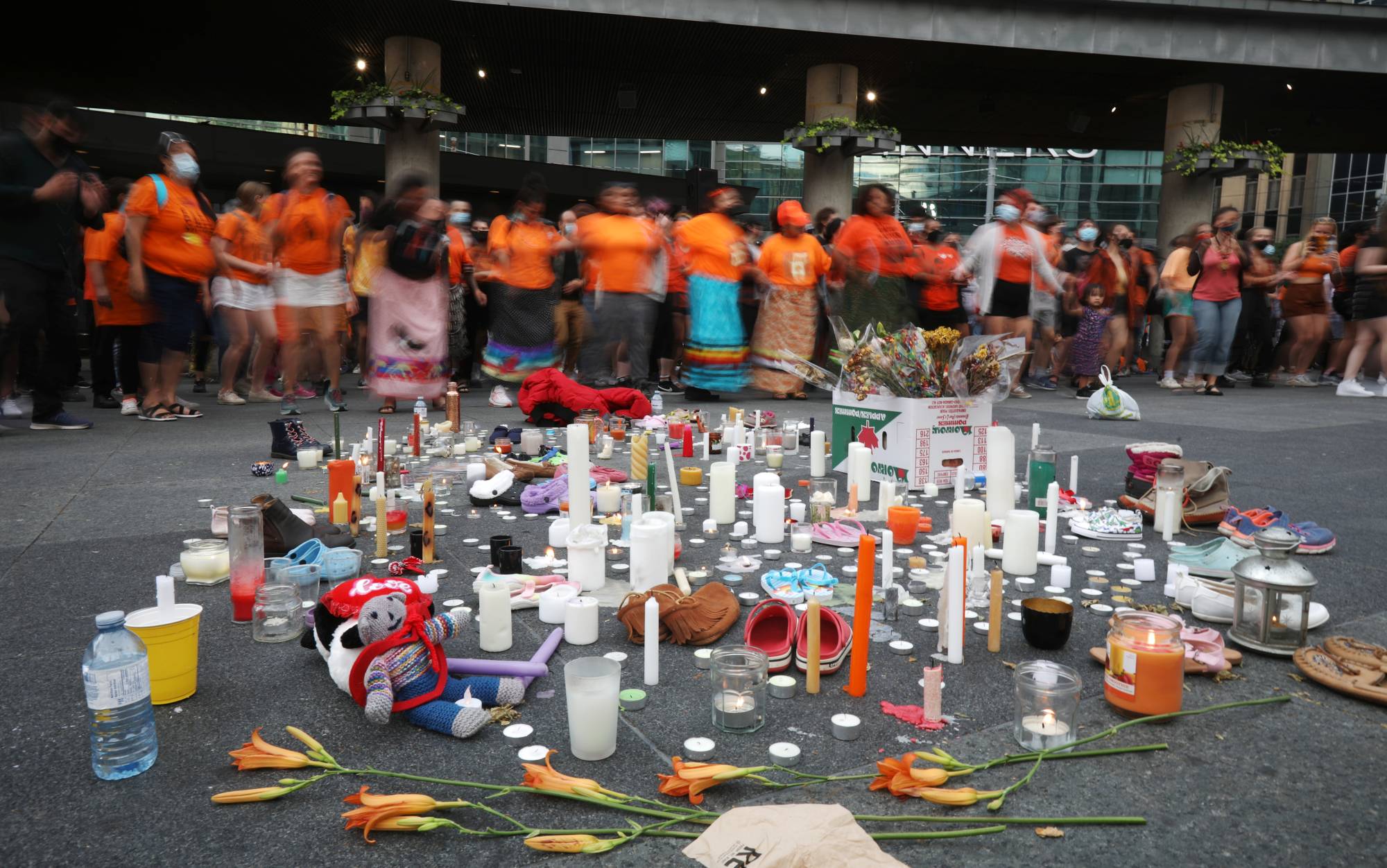 People participate in a round dance in front of candles and items placed on the ground in honor of the hundreds of remains of children discovered at former indigenous residential schools, on Thursday in Toronto. | Reuters