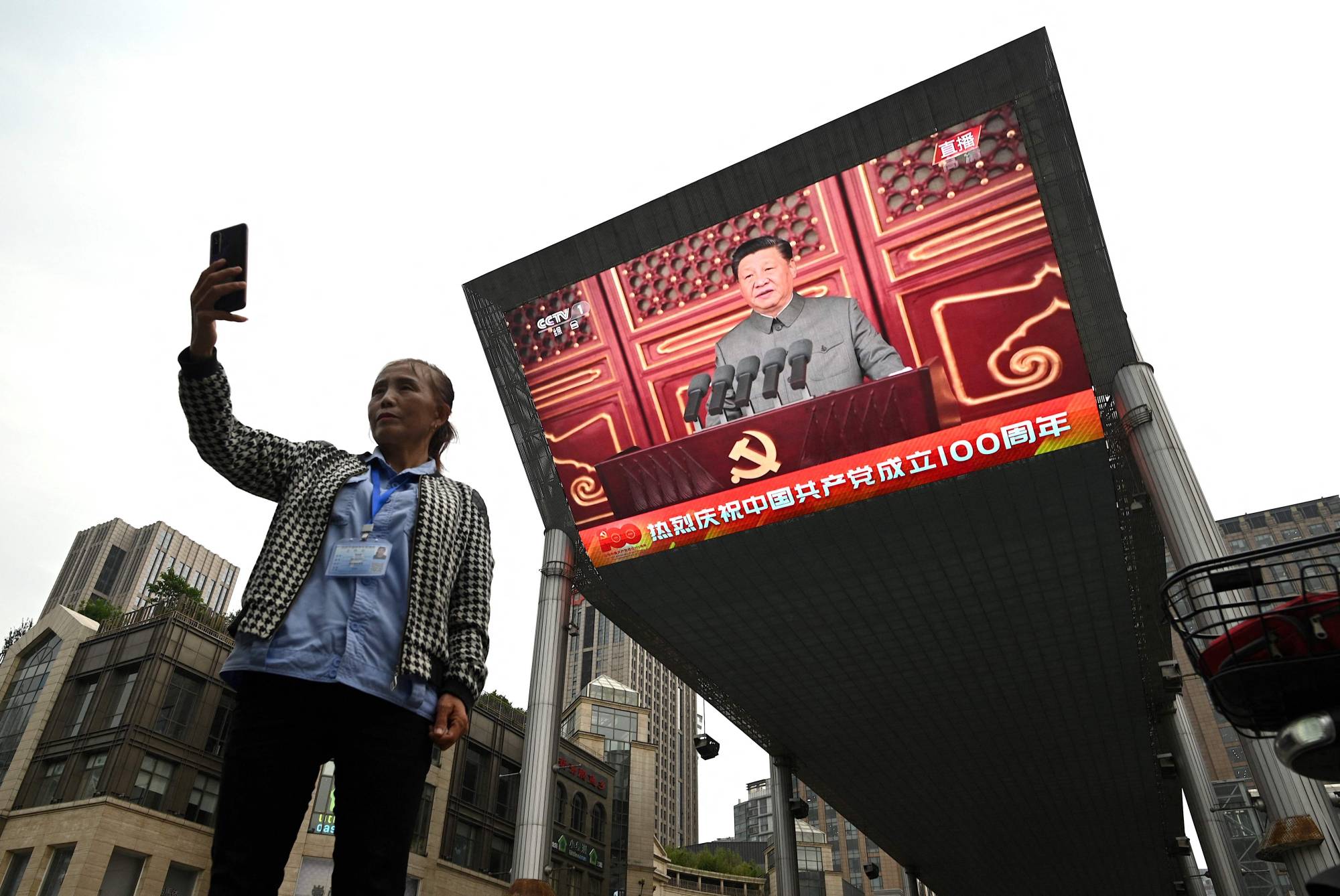 A woman takes a selfie as Chinese leader Xi Jinping's speech is broadcast on a large screen in Beijing on the 100th anniversary of the founding of the Communist Party of China on Thursday. | AFP-JIJI