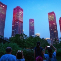 Chinese characters reading \"Never forget the original intention\" and the emblem of the Chinese Communist Party illuminate buildings during a light show in Beijing on June 26. | BLOOMBERG 