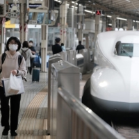 A passenger wearing a protective mask walks past a bullet train on a platform at Tokyo Station in the capital. East Japan Railway Co. said Tuesday it will inspect the belongings of some passengers during the Tokyo Olympics at major stations in the metropolitan area in cooperation with police, as part of measures to prevent crime and terrorism. | BLOOMBERG