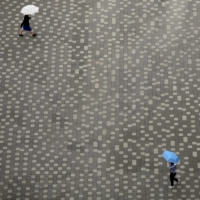 Socially distanced people, holding umbrellas in the rain, walk across a square in Tokyo\'s Koto Ward on Friday. | REUTERS