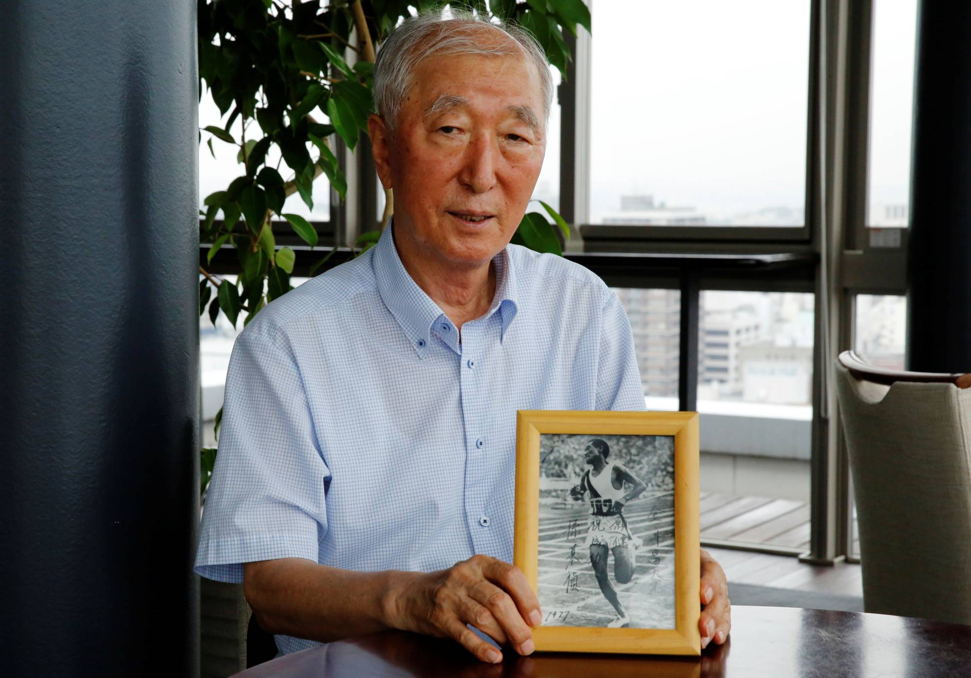 Son Chung-in poses with a photograph of his father, Sohn Kee-chung, who won the 1936 Berlin Olympics marathon, during an interview in Yokohama on July 8.  | REUTERS