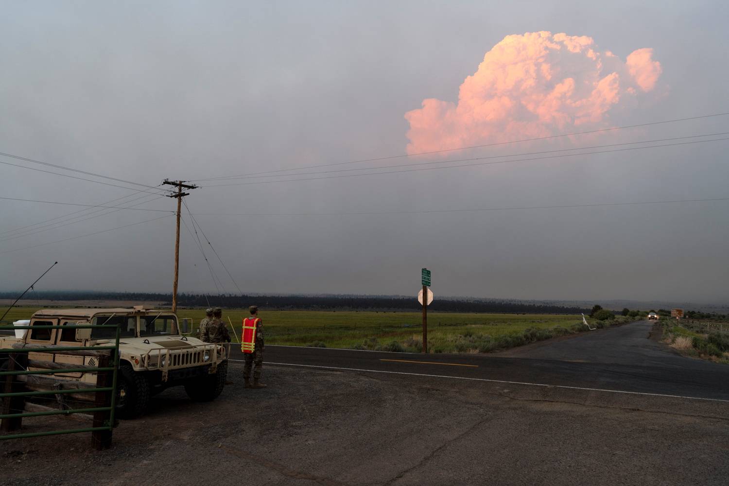 Members of the U.S. National Guard monitor a road blockade in Bly, Oregon, on Thursday as smoke from the Bootleg fire looms in the distance. | REUTERS