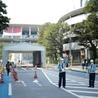 Guards marshal traffic on a blocked road in front of the National Stadium in early July, where restrictions have been put in place leading up to the opening ceremony of the Tokyo Games. | RYUSEI TAKAHASHI
