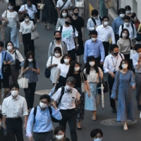 Evening commuters wearing protective face masks walk in Tokyo\'s Shinjuku Ward on Thursday. | BLOOMBERG