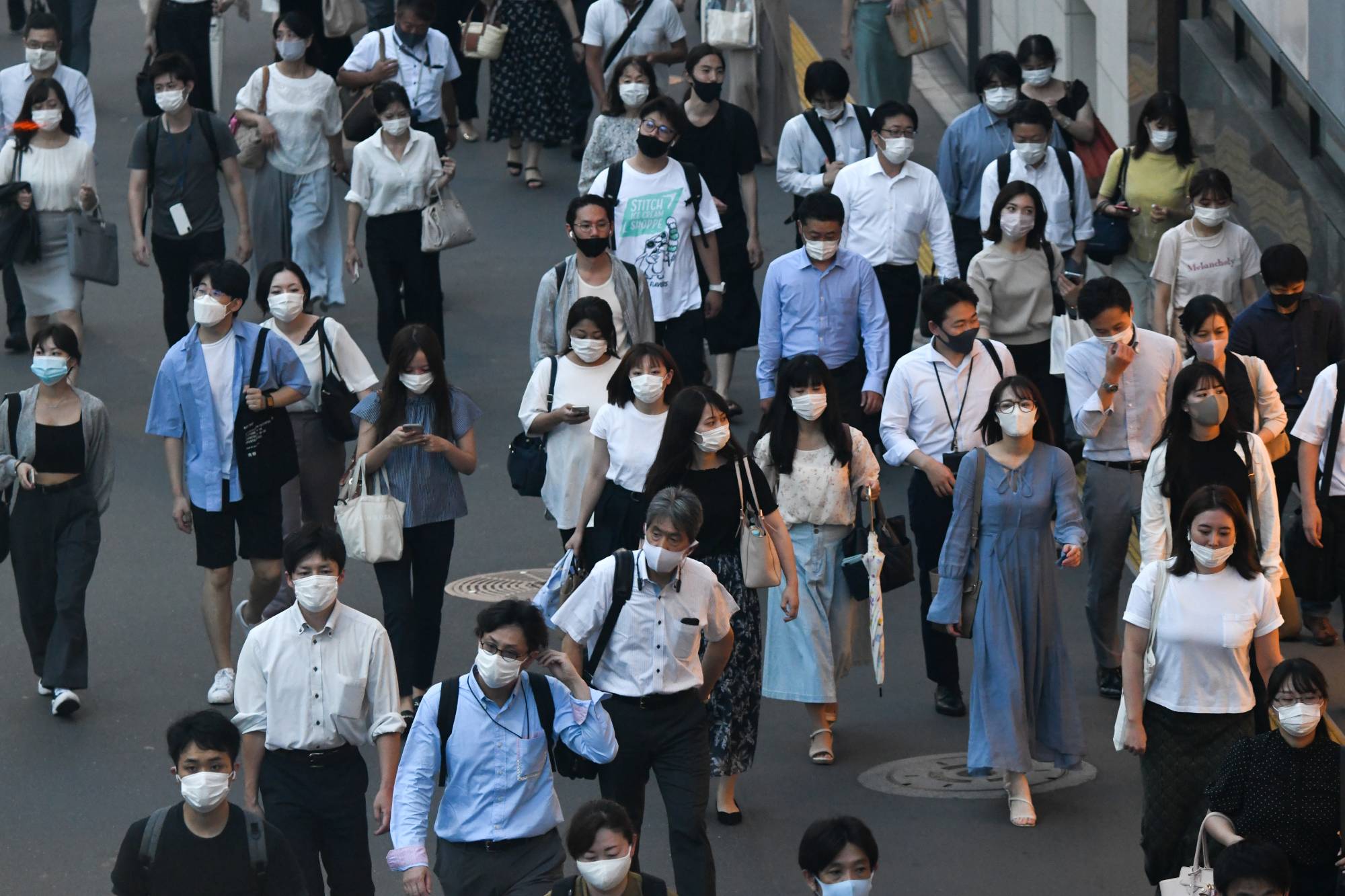 Evening commuters wearing protective face masks walk in Tokyo's Shinjuku Ward on Thursday. | Bloomberg