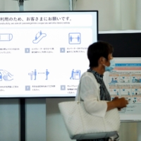 A woman walks past a disease prevention instructions board at Tokyo\'s Haneda Airport on Monday. | REUTERS